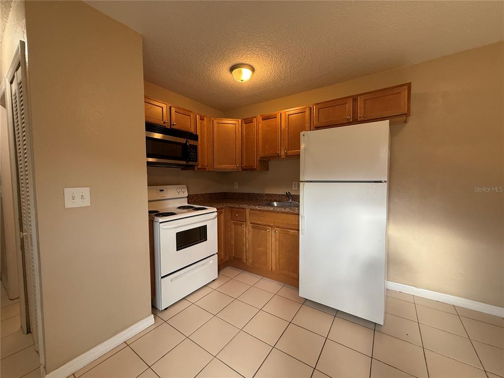 A kitchen with light wood cabinets, white appliances, and beige tile flooring — 601 HARDY STREET UNIT 8, BUNNELL, FL