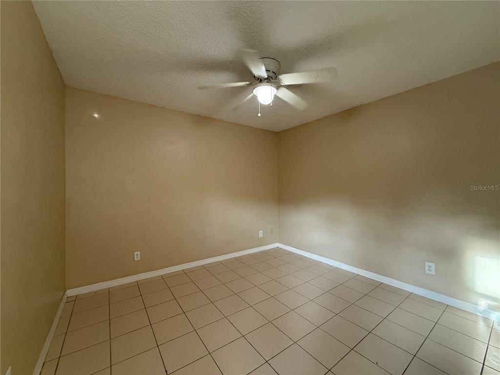 An empty bedroom features beige walls, a ceiling fan, and light-colored tile flooring — 601 HARDY STREET UNIT 8, BUNNELL, FL