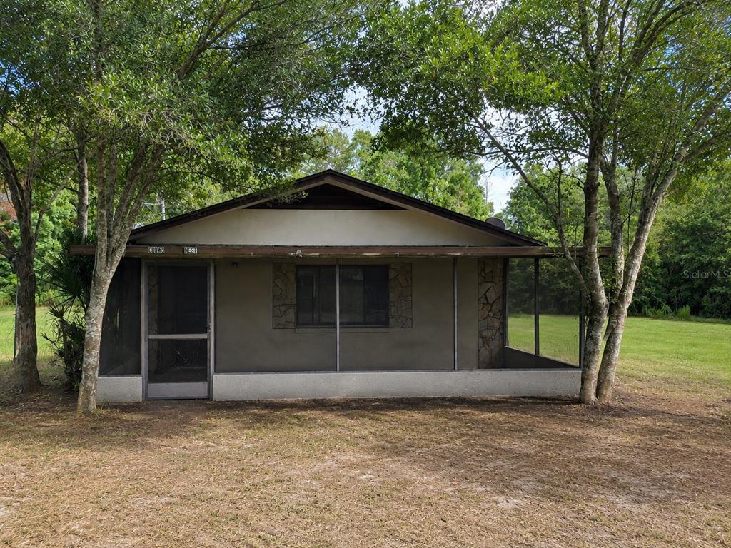 A small, single-story house with a screened-in front porch and stone accents sits outdoors — 5285 S HILLS POINT, LECANTO, FL