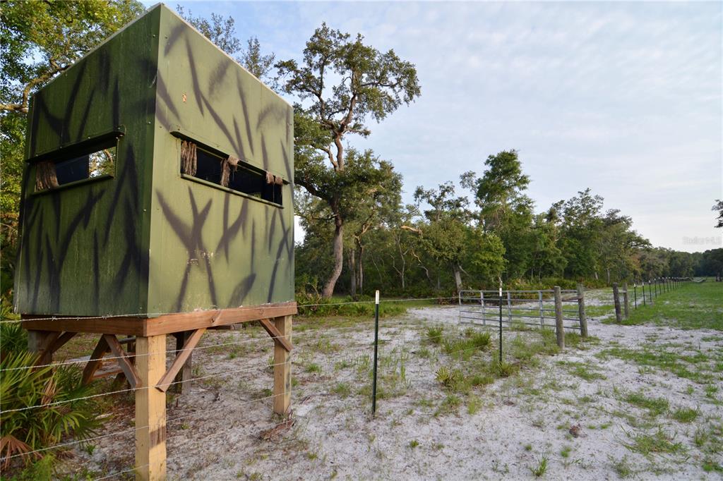 A camouflage hunting blind stands on wooden stilts in a sandy, fenced-in rural field — 2669 NW SUWANNEE VALLEY ROAD, LAKE CITY, FL