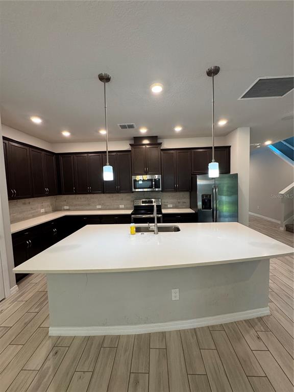 A kitchen features dark wood cabinets, white countertops, a large island, and light wood-look flooring — 4318 HIBISCUS BLOOM DRIVE, ORLANDO, FL