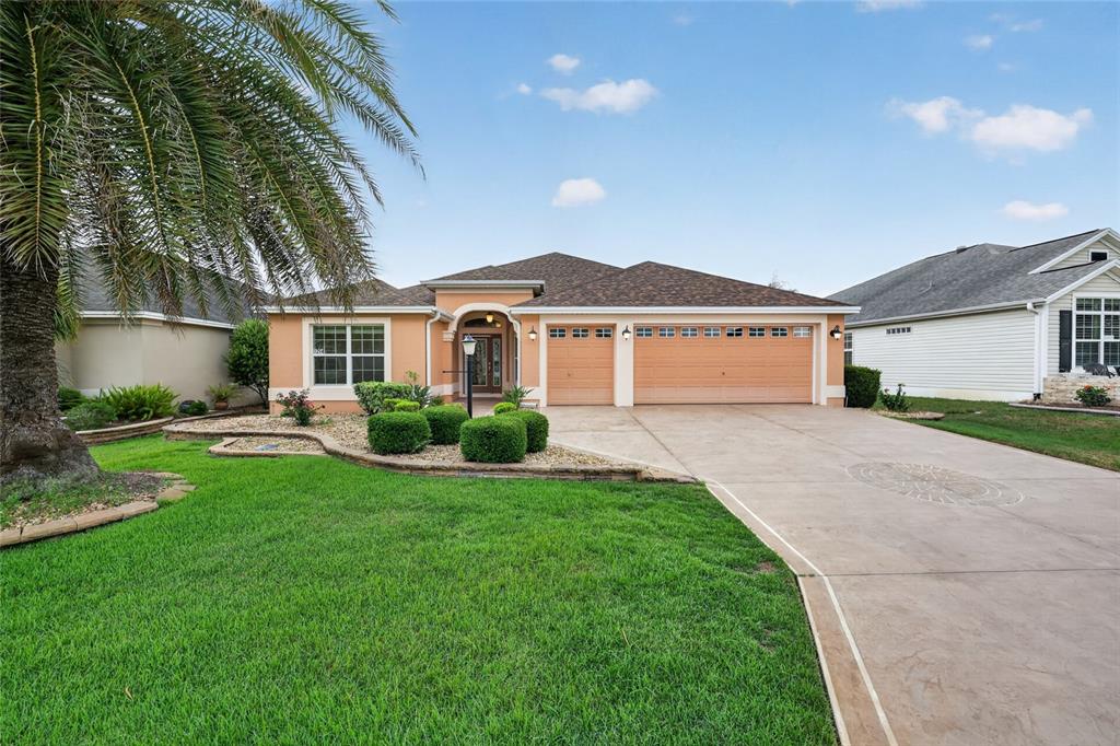 A single-story house with a tan stucco exterior, two garage doors, and a palm tree — 1294 ALLAIRE LOOP, THE VILLAGES, FL