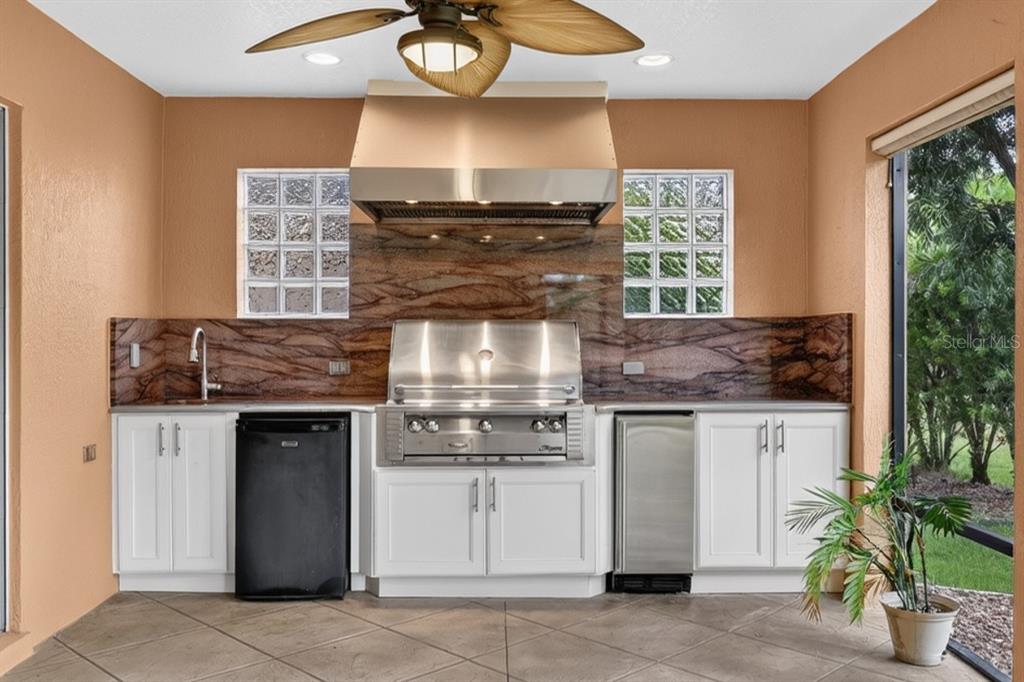An outdoor kitchen features white cabinets, a stainless steel grill, and a brown stone backsplash — 1294 ALLAIRE LOOP, THE VILLAGES, FL