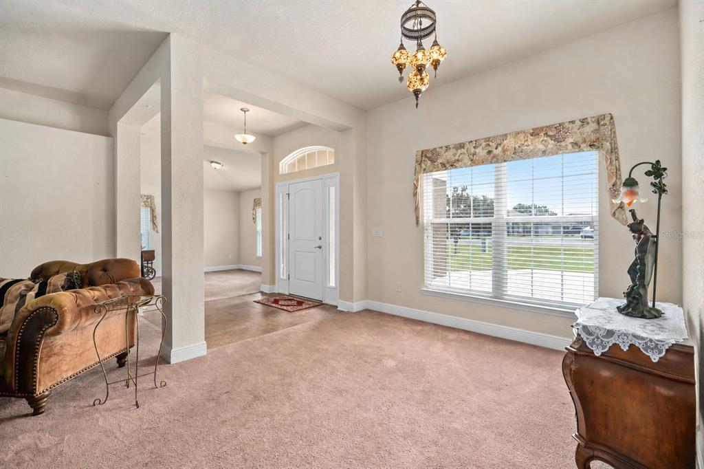 A carpeted living room features a chandelier, a large window, and an entryway with columns — 9558 SW 50TH COURT, OCALA, FL