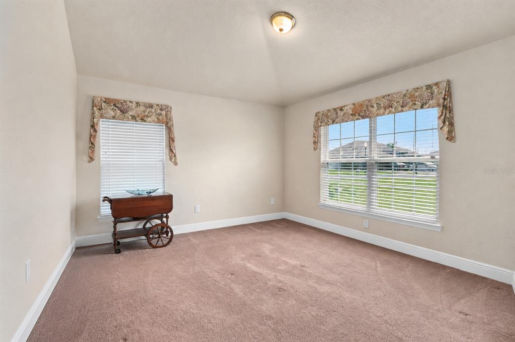 An empty bedroom with beige carpet, two windows with floral valances, and a wooden cart — 9558 SW 50TH COURT, OCALA, FL