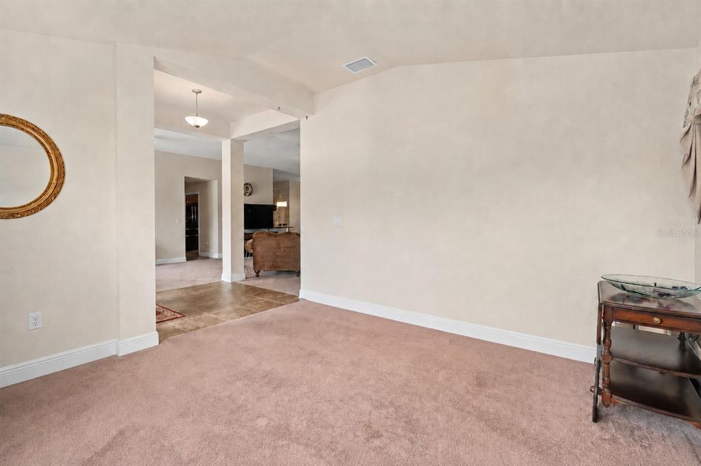 A carpeted living room features a large wall, a side table, and a view into another room — 9558 SW 50TH COURT, OCALA, FL