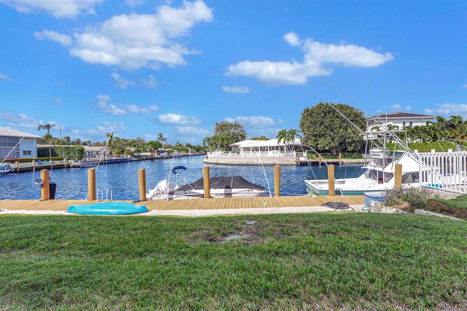 A grassy lawn overlooks a canal with a wooden dock, two boats, and waterfront homes — 2311 NE 36th Street # 1f, Lighthouse Point FL 33064, LIGHTHOUSE POINT, FL