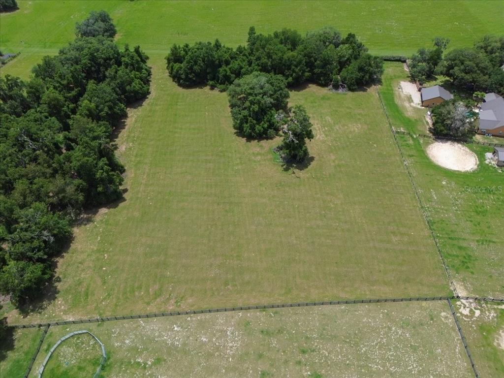 An aerial view shows a large, fenced, grassy lot with scattered trees and nearby buildings — TBD SW BLUEBIRD COURT, FORT WHITE, FL