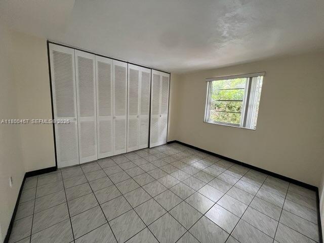 An empty room features white louvered closet doors, light-colored tile flooring, and a single window — 7125 Dickens Ave # 4, Miami Beach FL 33141, MIAMI BEACH, FL