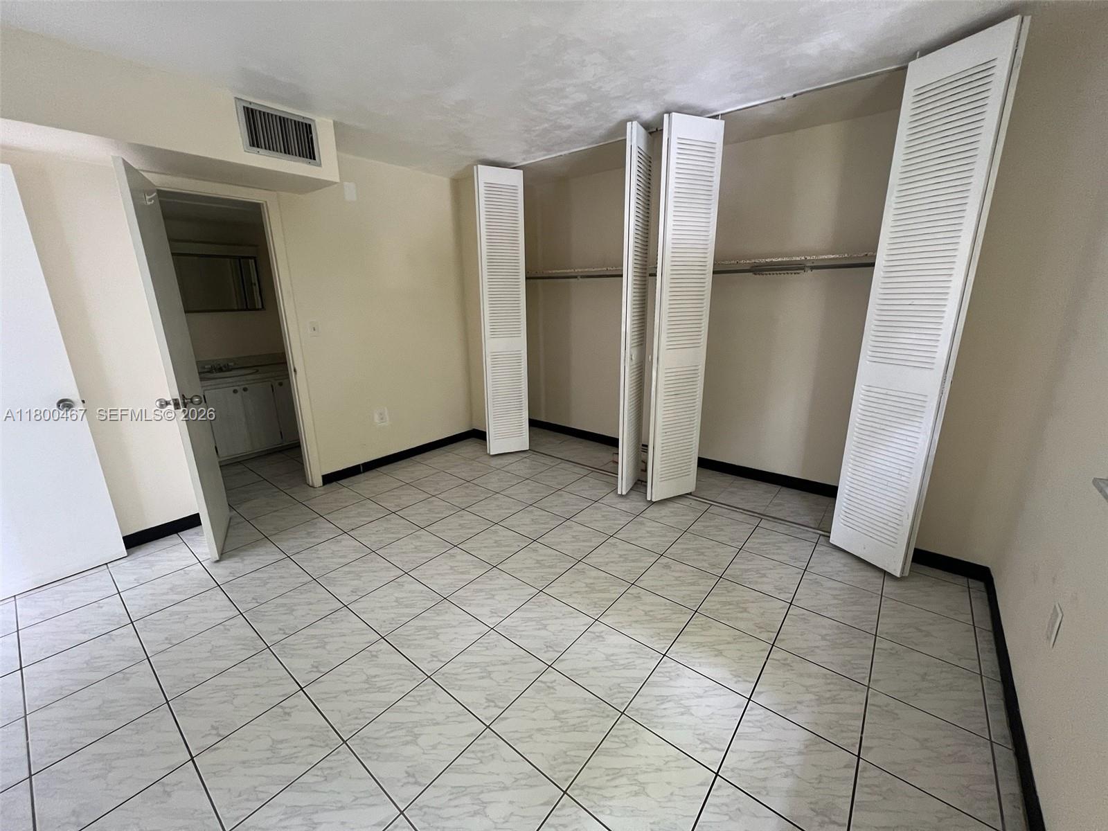 A room with white tiled floors, louvered closet doors, and an adjacent bathroom doorway — 7125 Dickens Ave # 4, Miami Beach FL 33141, MIAMI BEACH, FL