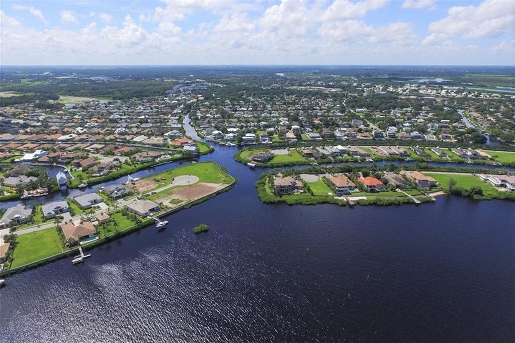 An aerial view shows waterfront houses along canals in a residential neighborhood under a blue sky — 4747 PINNACLE DRIVE, BRADENTON, FL