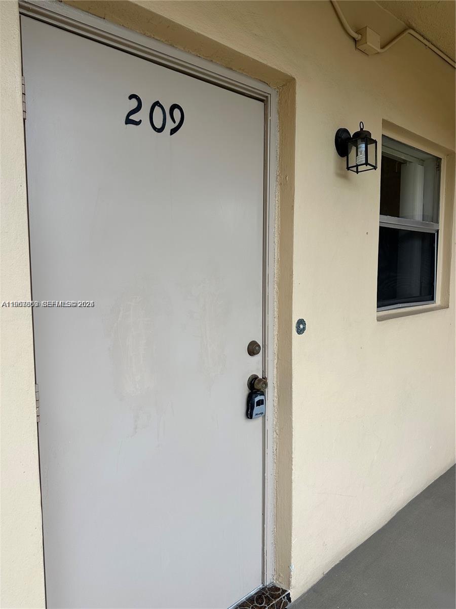 A light-colored exterior door labeled 209 features a lockbox and an adjacent wall-mounted light fixture — 200 Ashbury Rd # 209, Hollywood FL 33024, HOLLYWOOD, FL