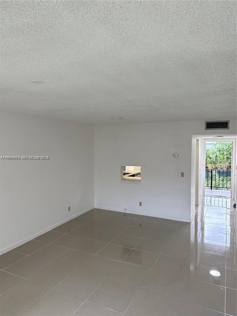 An empty room features light-colored tile flooring, white walls, and a doorway leading to a balcony — 200 Ashbury Rd # 209, Hollywood FL 33024, HOLLYWOOD, FL
