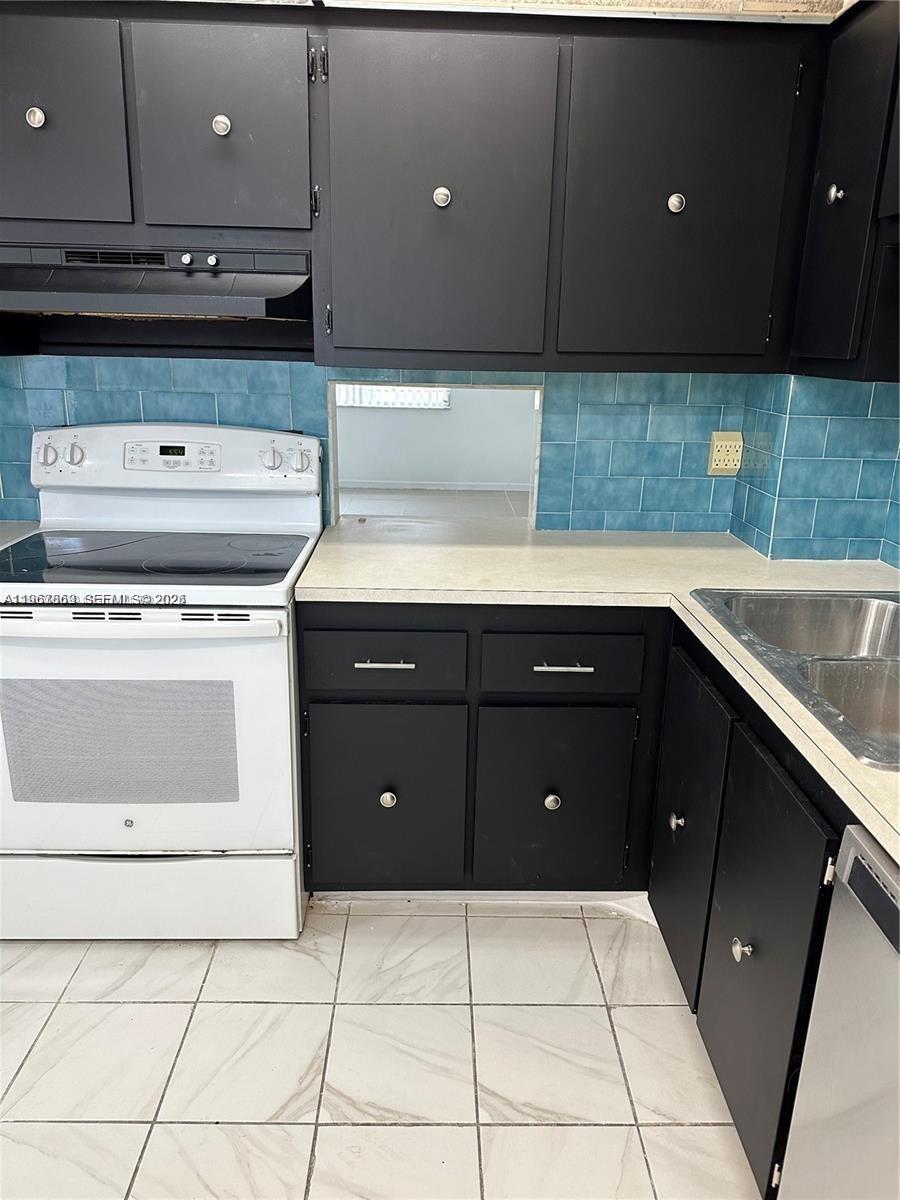 A kitchen features black cabinets, a white stove, blue tile backsplash, and light-colored countertops — 200 Ashbury Rd # 209, Hollywood FL 33024, HOLLYWOOD, FL
