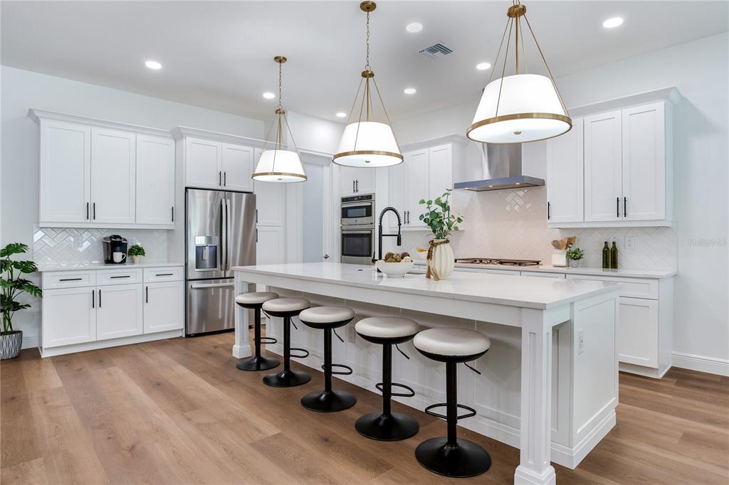 A modern kitchen features white cabinetry, a large center island with bar stools, and stainless appliances — 2814 54TH STREET S, GULFPORT, FL