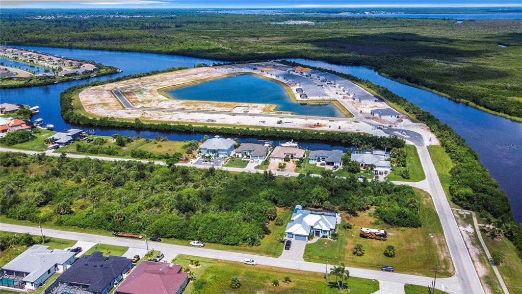 An aerial view shows a residential neighborhood with a large central pond under construction — 15707 MARGO CIRCLE, PORT CHARLOTTE, FL