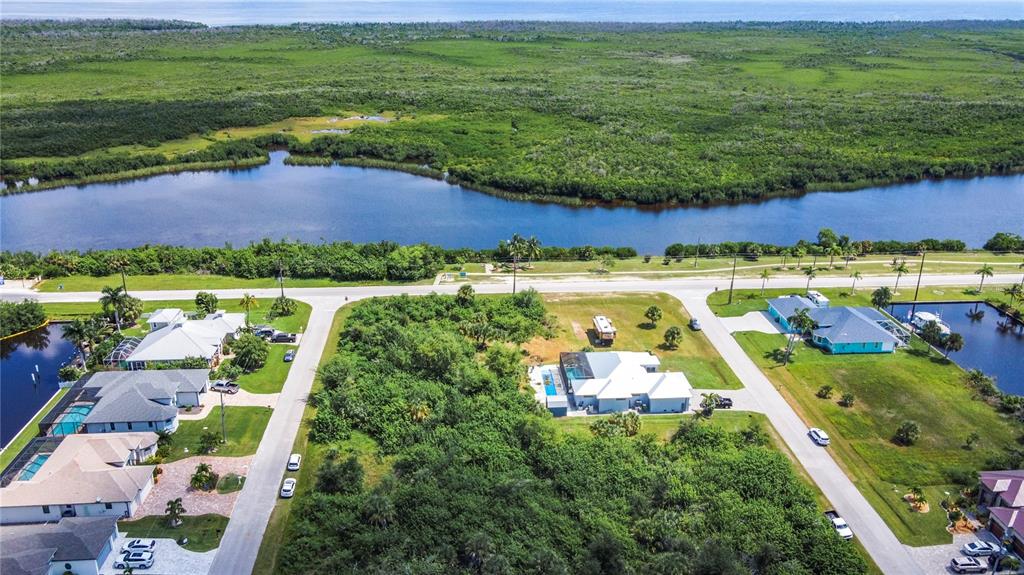An aerial view shows houses, a large wooded lot, and a canal near the coast — 15707 MARGO CIRCLE, PORT CHARLOTTE, FL