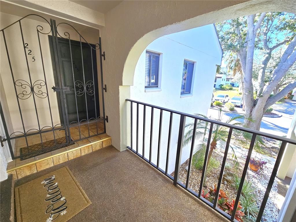 An outdoor balcony features a metal security gate, a welcome mat, and a black railing — 812 CAPRI ISLES BOULEVARD UNIT 225, VENICE, FL