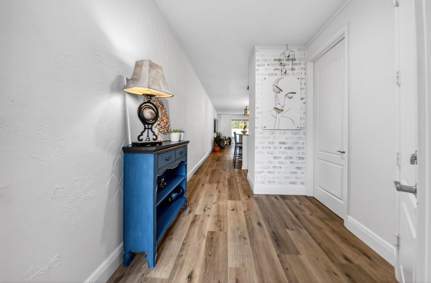 A hallway features wood-look flooring, a blue console table with a lamp, and white walls — 1942 NE 32nd Street, Lighthouse Point FL 33064, LIGHTHOUSE POINT, FL