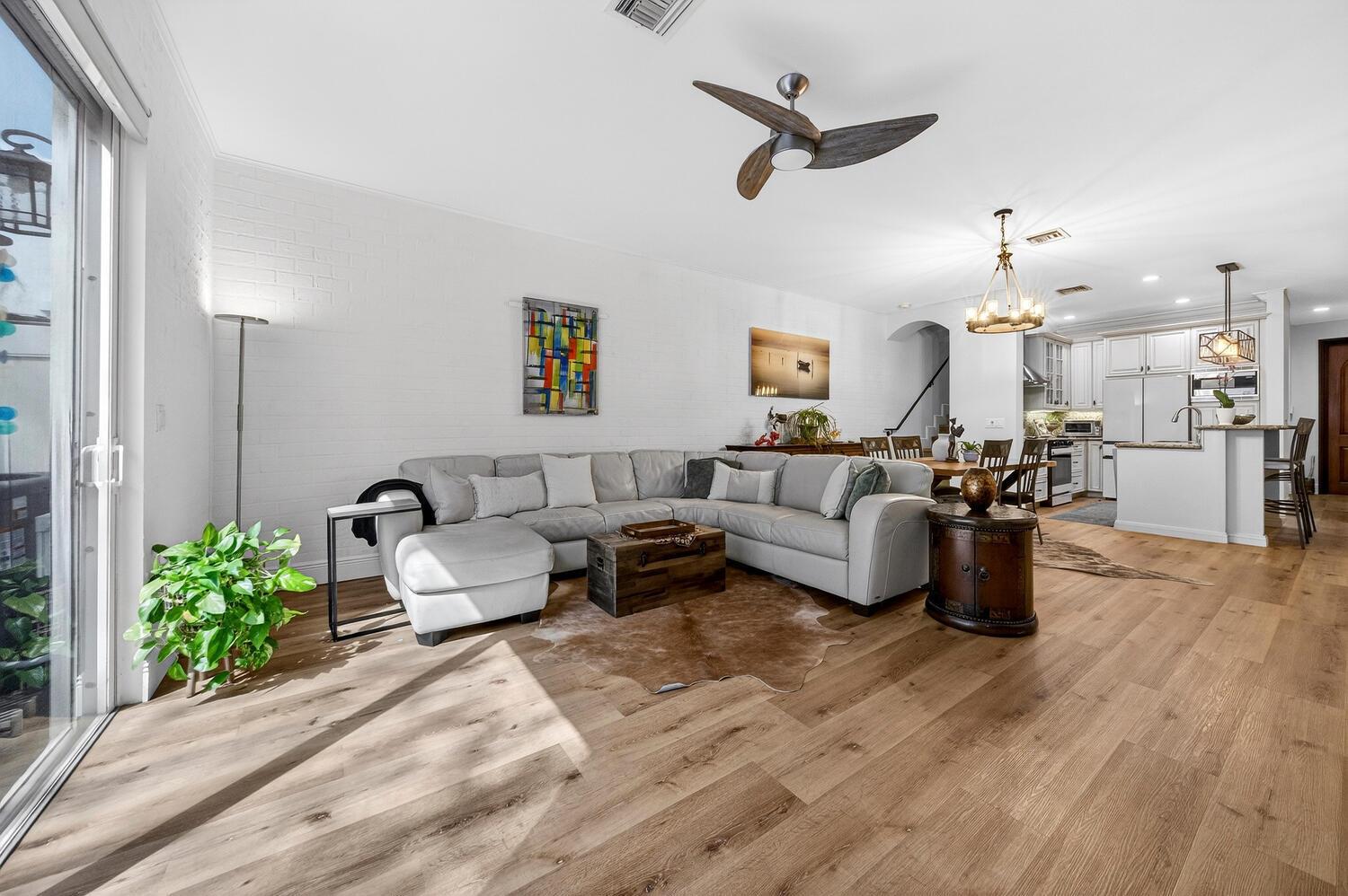 A living room with a light gray sectional, wood flooring, and an open kitchen area — 1942 NE 32nd Street, Lighthouse Point FL 33064, LIGHTHOUSE POINT, FL