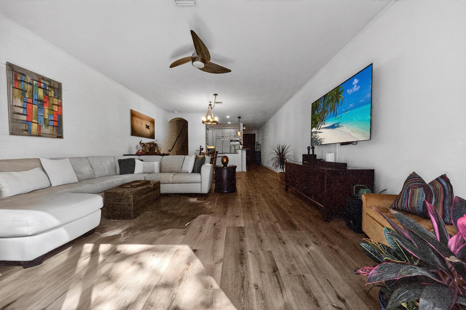 A living room with light wood floors, a white sectional sofa, and a wall-mounted television — 1942 NE 32nd Street, Lighthouse Point FL 33064, LIGHTHOUSE POINT, FL