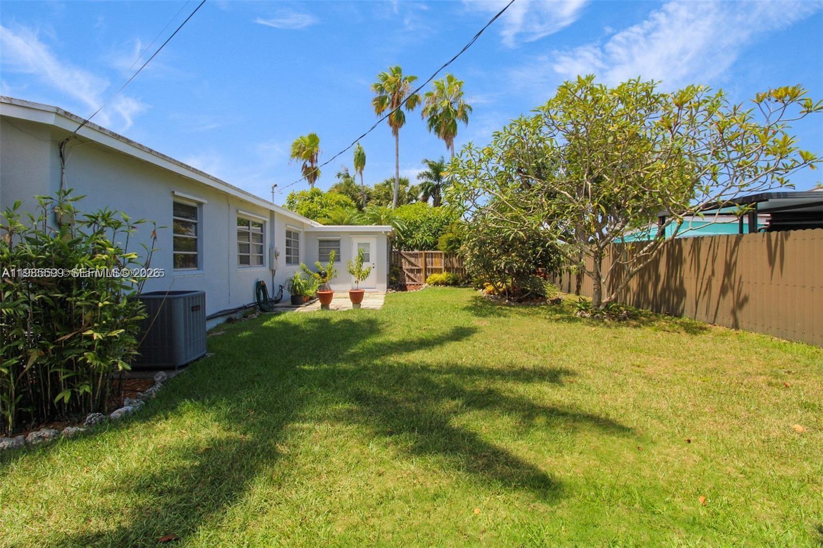 A grassy backyard features a light-colored house exterior, a patio area, and a wooden fence — 10250 Caribbean Blvd, Cutler Bay FL 33189, CUTLER BAY, FL