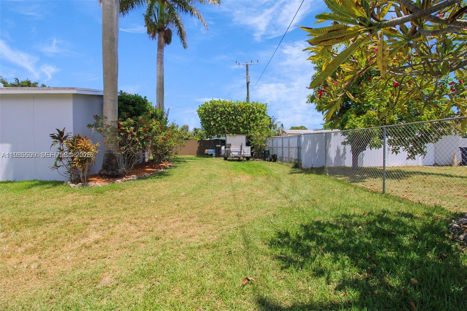 A grassy backyard features a chain-link fence, palm trees, and a utility trailer — 10250 Caribbean Blvd, Cutler Bay FL 33189, CUTLER BAY, FL