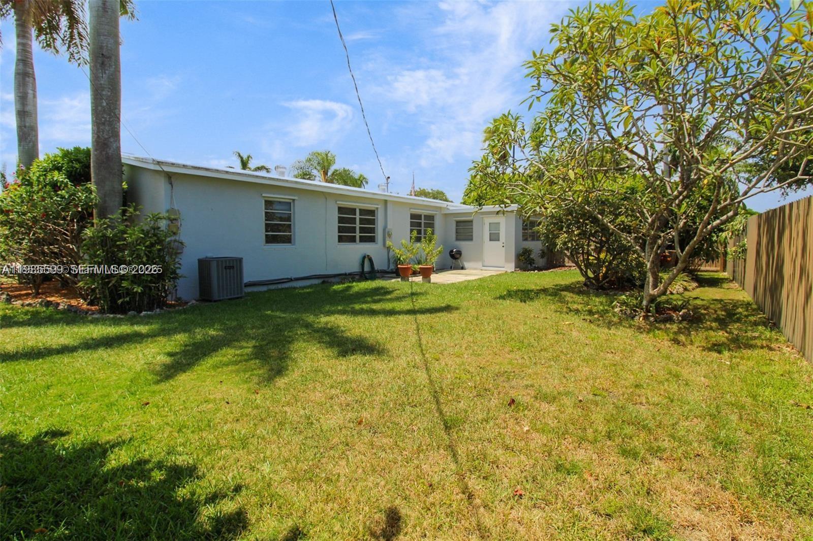 A backyard view of a single-story house with a lawn, trees, and a wooden fence — 10250 Caribbean Blvd, Cutler Bay FL 33189, CUTLER BAY, FL