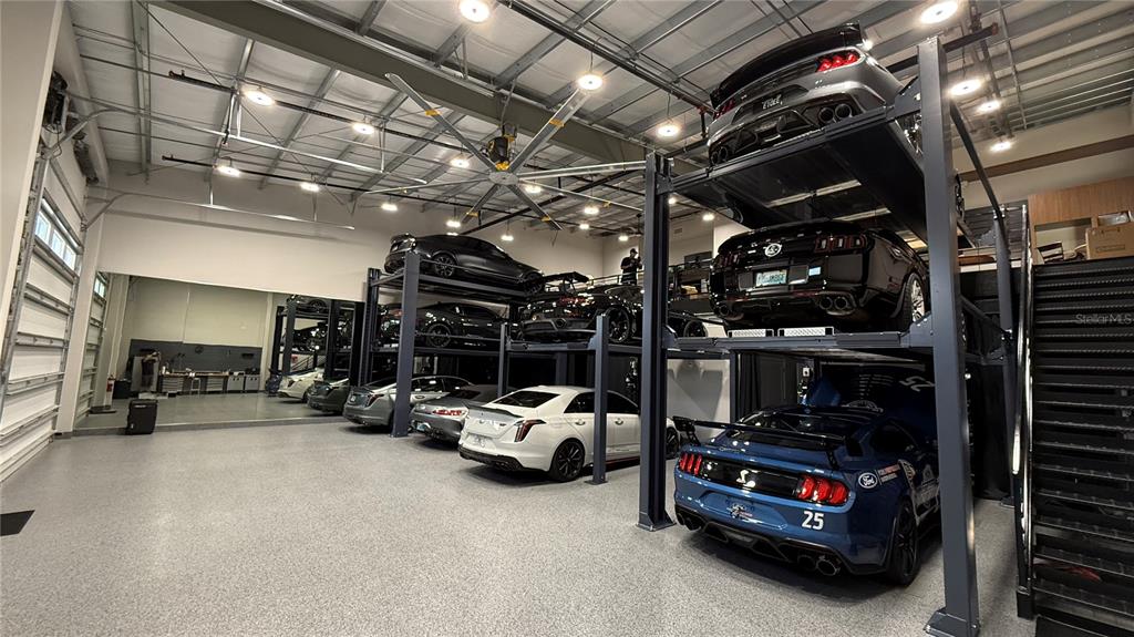 A spacious garage features multiple car lifts, epoxy flooring, and several parked luxury vehicles — 8185 APEX WAY, SEBRING, FL