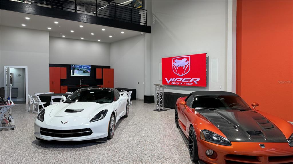 A spacious garage features a white Corvette, an orange Dodge Viper, and a large display screen — 8185 APEX WAY, SEBRING, FL