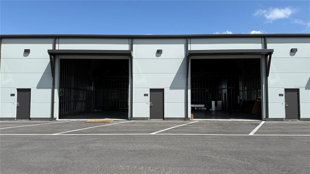 The exterior of a commercial building features three dark doors and two large open bays — 8185 APEX WAY, SEBRING, FL