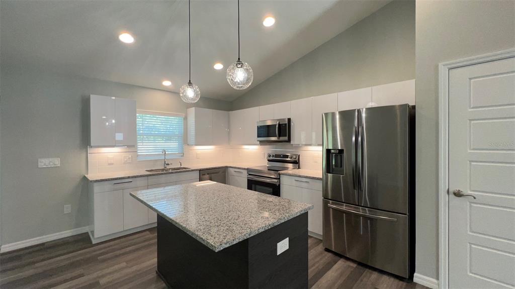 A modern kitchen features white cabinets, granite countertops, a dark island, and stainless steel appliances — TBD FISHER LANE TRACE, OCKLAWAHA, FL