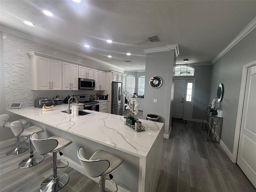 A modern kitchen features white cabinetry, quartz countertops, a breakfast bar, and gray flooring — 5028 OLDE KERRY DRIVE, ORLANDO, FL