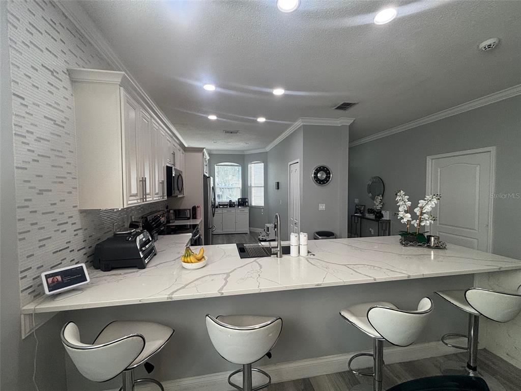 A kitchen features white cabinets, a quartz island with bar seating, and gray walls — 5028 OLDE KERRY DRIVE, ORLANDO, FL