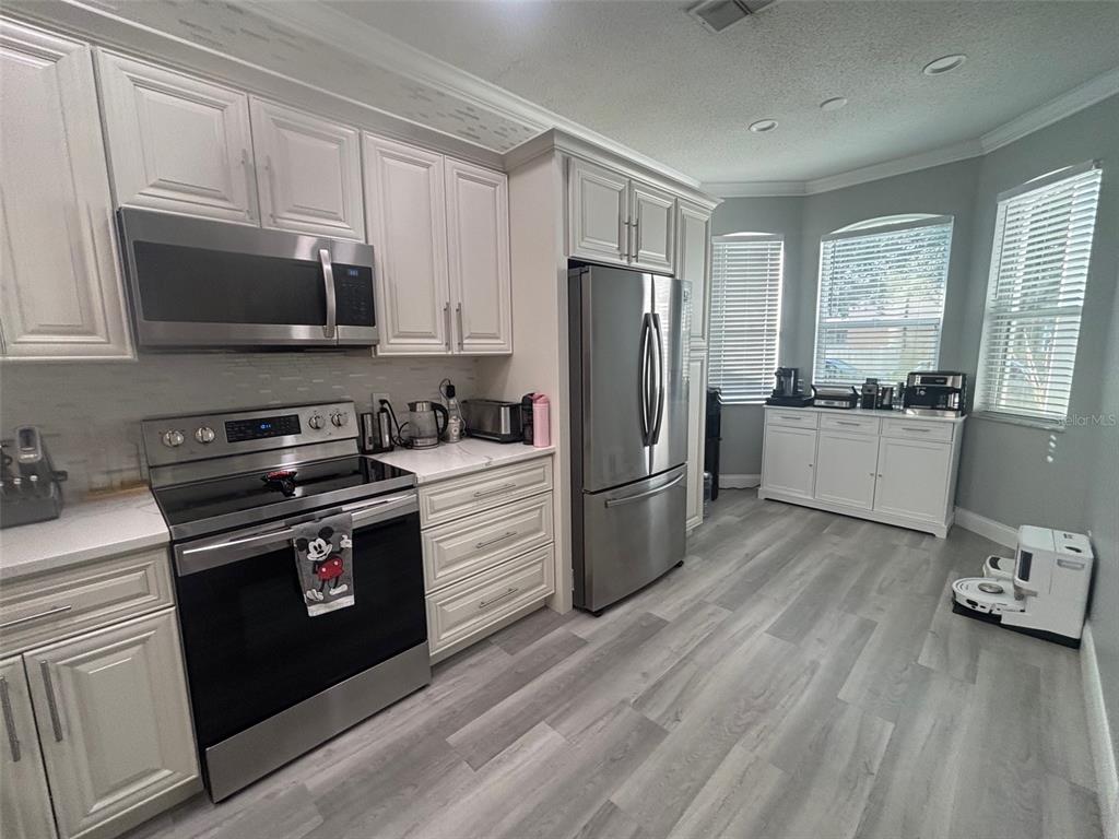 A kitchen features white cabinets, stainless steel appliances, and light wood-look flooring — 5028 OLDE KERRY DRIVE, ORLANDO, FL