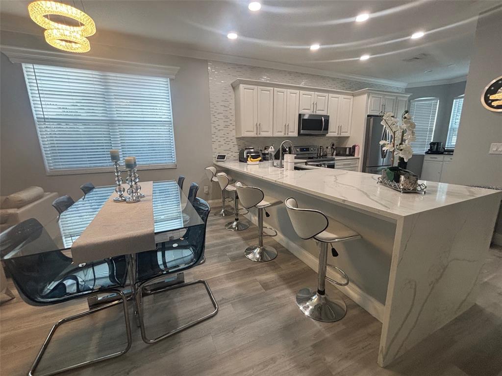 A kitchen and dining area with white cabinetry, marble-look countertops, and modern bar stools — 5028 OLDE KERRY DRIVE, ORLANDO, FL