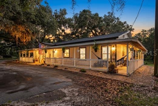 A single-story house with a wrap-around porch sits under large trees at dusk — 3551 NW 60TH AVENUE, CHIEFLAND, FL