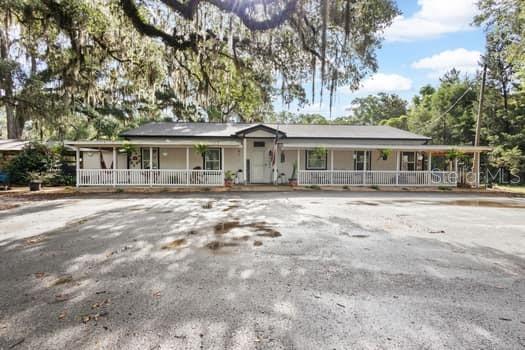 A single-story house with a long front porch and white railing sits on a gravel lot — 3551 NW 60TH AVENUE, CHIEFLAND, FL