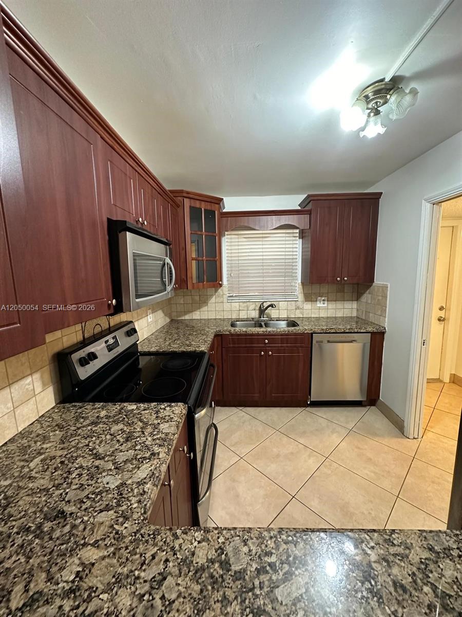 A kitchen features dark wood cabinets, granite countertops, stainless steel appliances, and tile flooring — 9410 Live Oak Pl # 305, Davie FL 33324, DAVIE, FL