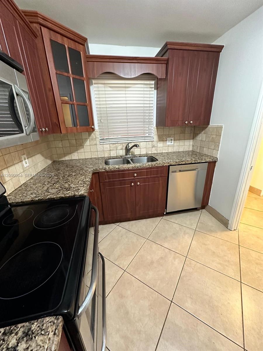 A kitchen features wood cabinets, granite countertops, a stainless steel dishwasher, and tile flooring — 9410 Live Oak Pl # 305, Davie FL 33324, DAVIE, FL