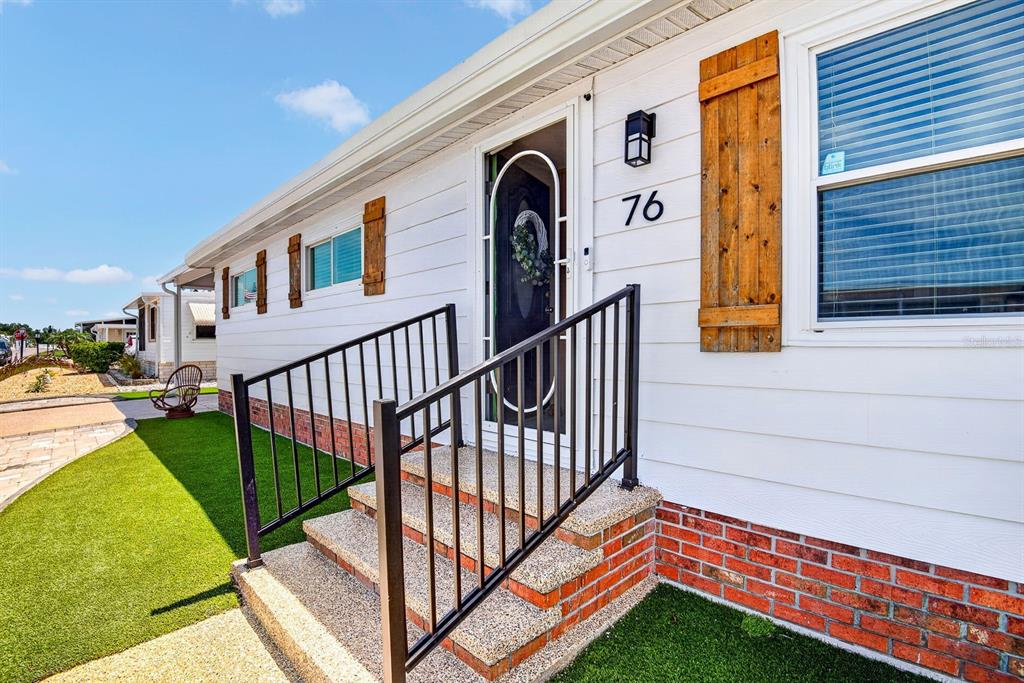 A white mobile home exterior features a brick base, front steps with railings, and shutters — 76 CABALLO WAY, BRADENTON, FL