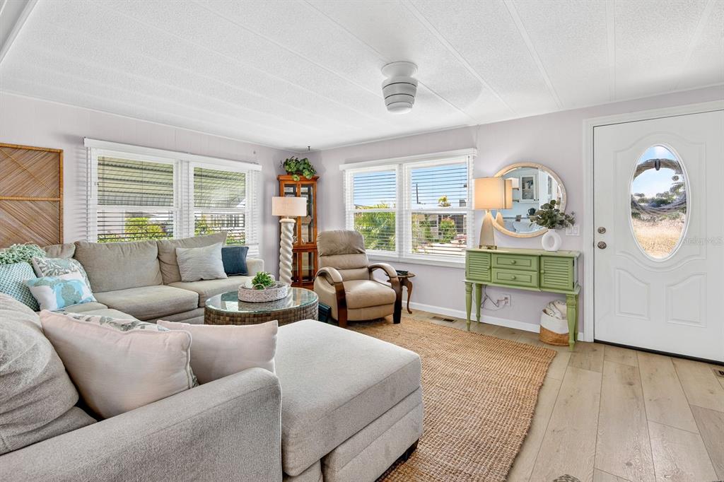 A living room features a sectional sofa, a recliner, a green console table, and windows — 76 CABALLO WAY, BRADENTON, FL