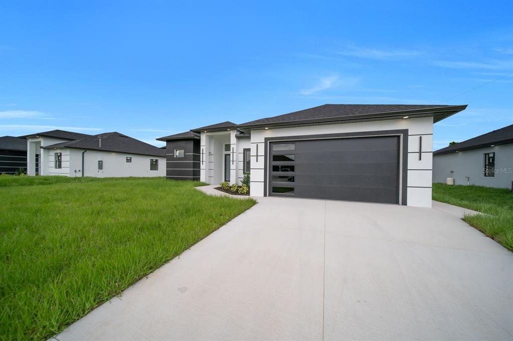 A modern single-story house with a white exterior, dark garage door, and a concrete driveway — 3618 6TH STREET SW, LEHIGH ACRES, FL