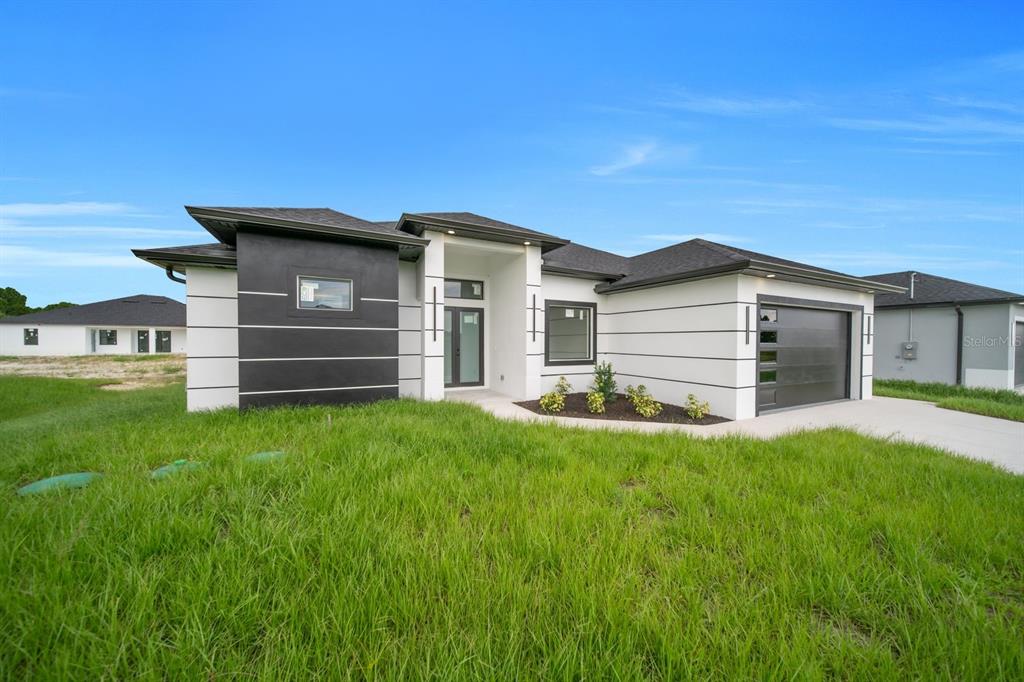A modern single-story house with a black and white exterior, a garage, and a lawn — 3618 6TH STREET SW, LEHIGH ACRES, FL