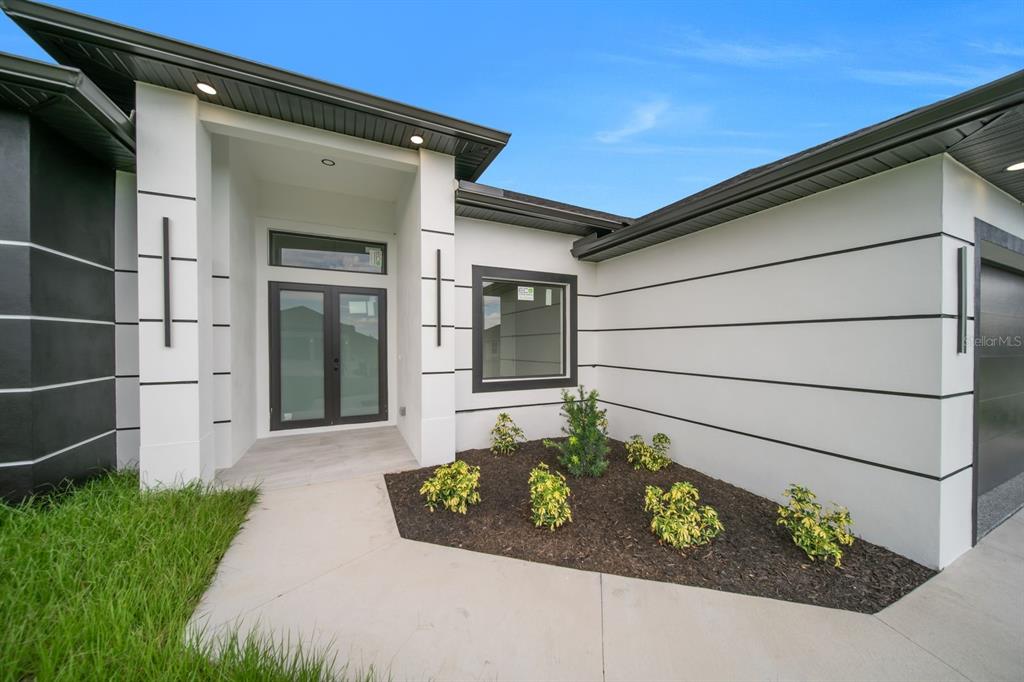 A modern house exterior features white walls with horizontal black accents and a covered entryway — 3618 6TH STREET SW, LEHIGH ACRES, FL