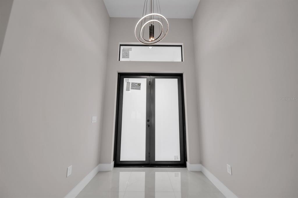 A modern entryway features double glass doors, a transom window, and a circular pendant light — 3618 6TH STREET SW, LEHIGH ACRES, FL