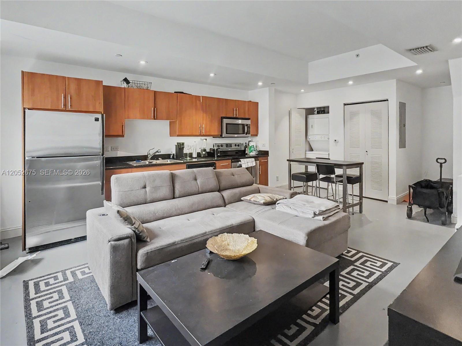 A modern open-concept living area features a kitchen with wood cabinets and a gray sectional — 111 E Flagler St # 410, Miami FL 33131, MIAMI, FL