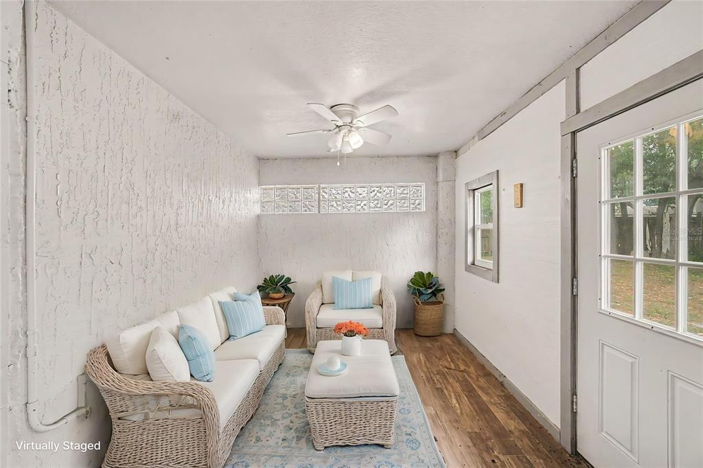A sunroom features a white sofa, armchair, ottoman, glass block windows, and wood-look flooring — 890 DELAND AVENUE, ORANGE CITY, FL