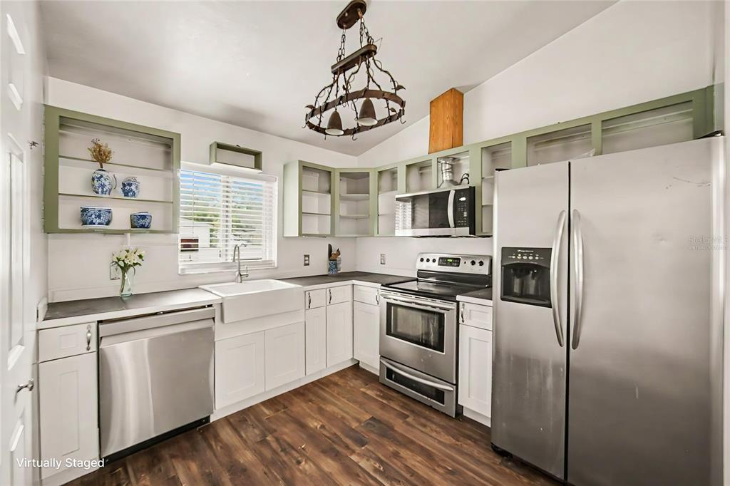 A kitchen with white cabinets, sage green open shelving, stainless steel appliances, and wood flooring — 890 DELAND AVENUE, ORANGE CITY, FL
