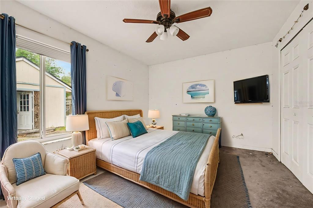 A bedroom features a rattan bed, blue dresser, wall-mounted television, and a window with curtains — 890 DELAND AVENUE, ORANGE CITY, FL